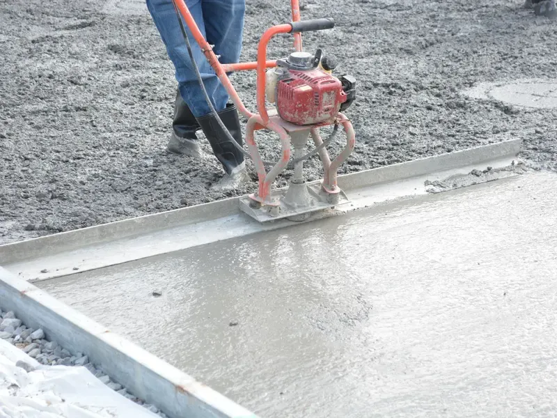 Worker running a power trowel over a freshly poured concrete slab
