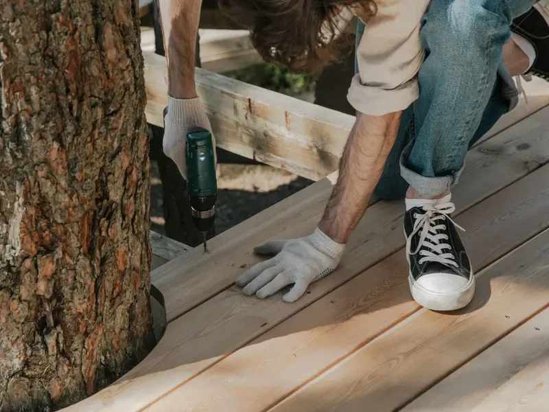 Worker drilling a screw into a deck board next to a tree