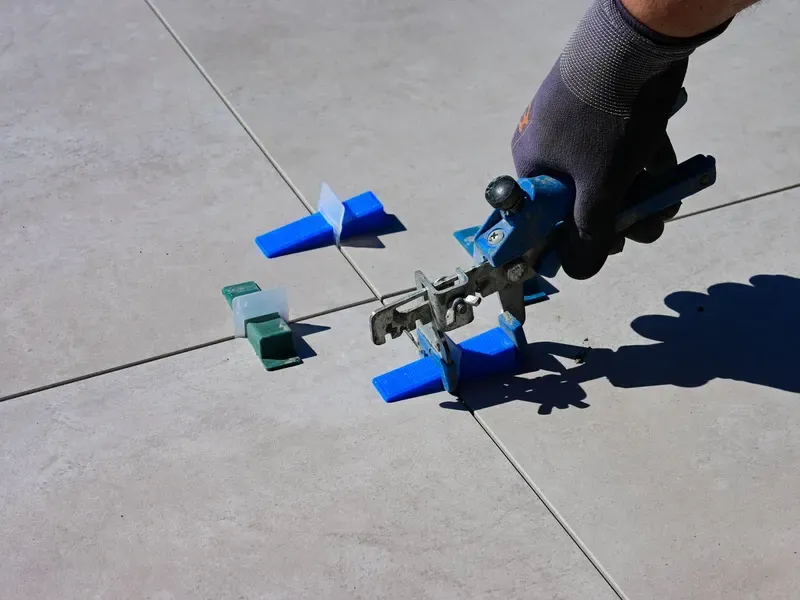 Gloved hand using a tile leveling clip system on a tiled floor
