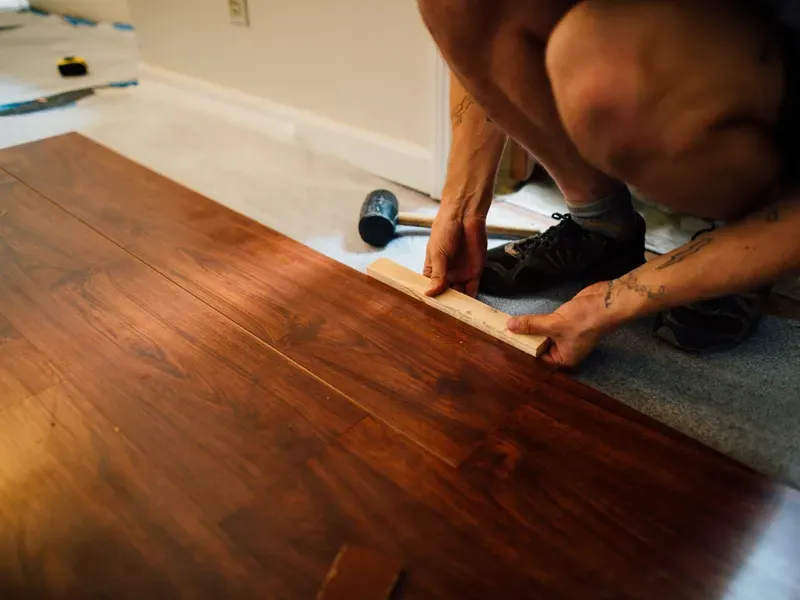 Installer using a mallet and tapping block to fit laminate flooring