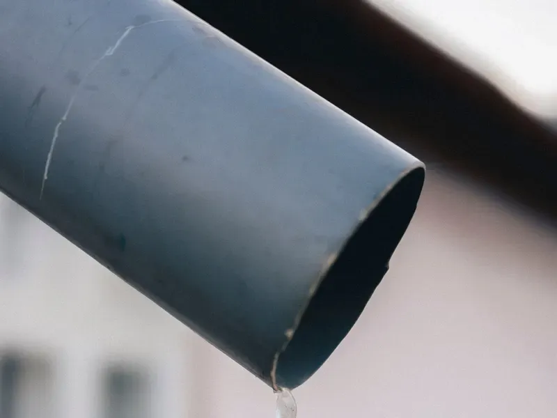 Icicle forming at the end of a metal gutter downspout in winter