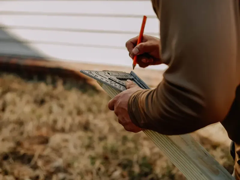 Carpenter using a speed square and pencil to mark a board outdoors